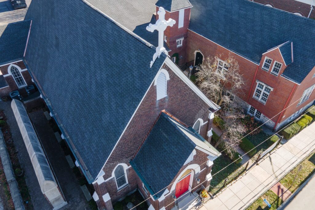Aerial view of a dark asphalt shingle roof on a large brick church